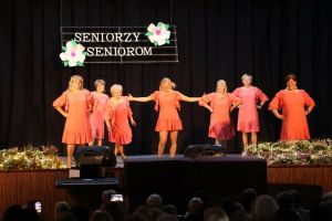 Grupa seniorek tańcząca na scenie z instruktorką